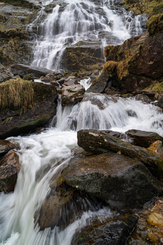 Cascading waterfall flowing over moss-covered rocks in a forested stream.