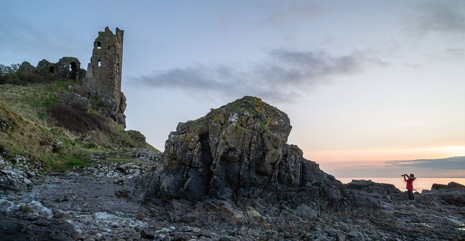 Ruined stone tower on a hilltop beside a large rocky outcrop at twilight.