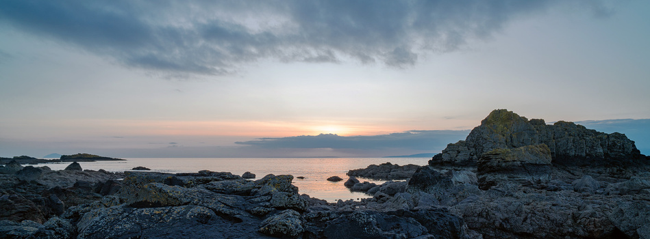 Rocky coastline at sunset with calm water and dramatic cloudy sky.
