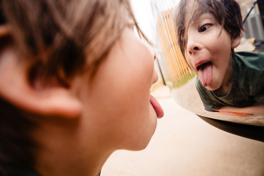 Child's face in profile with tongue out, reflected in a mirror with warm, soft lighting.