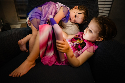 Two young girls playing together on a dark floor, wearing colorful clothing with vibrant pink and purple fabrics in motion.