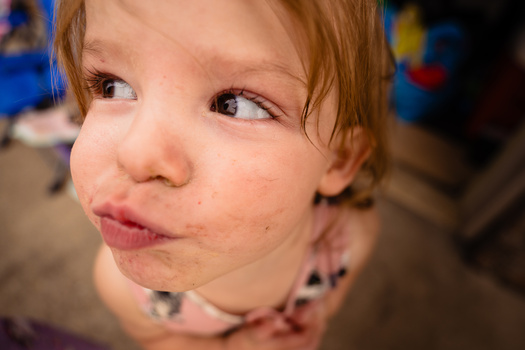 Young child with reddish hair making an exaggerated facial expression, looking upward with pursed lips.