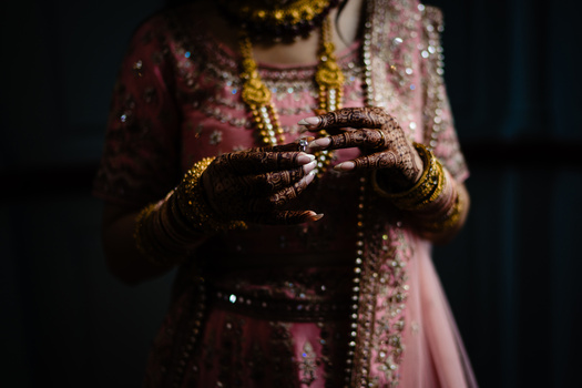 Bride's hands adorned with ornate henna, gold bangles, and jewelry holding a beaded string.
