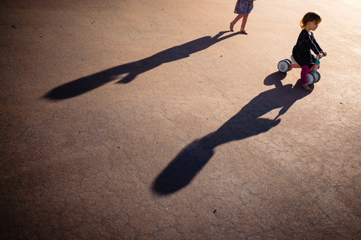 Two children playing on pavement with long shadows cast by afternoon sunlight.