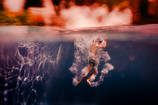 Underwater split-view showing a person suspended beneath the surface with bubbles and ethereal lighting above the waterline.