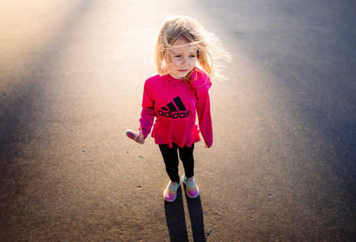 Young child running toward camera on a paved surface, backlit by golden sunlight with lens flare.
