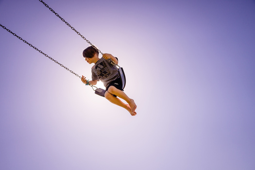 Person suspended mid-air on a rope swing against a clear purple sky.