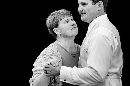 Man in white shirt embracing woman from behind against black background.