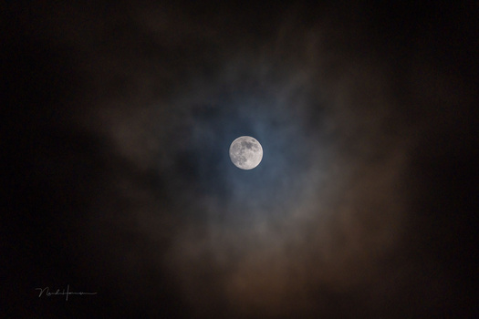 Full moon surrounded by dark, layered clouds in night sky.