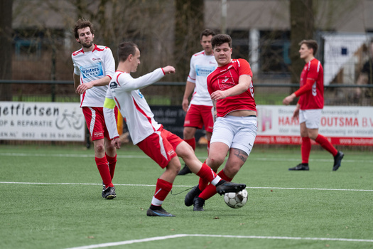 Young soccer player in red jersey controls ball while being defended during outdoor match.