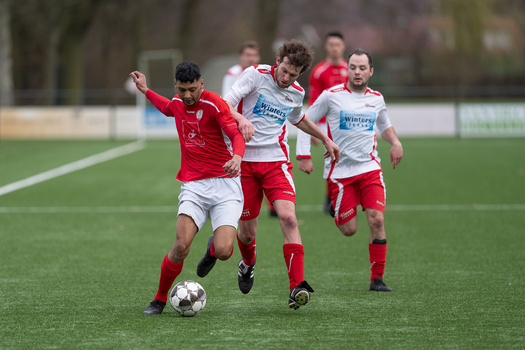 Youth soccer player in red jersey controls ball while opponent in white jersey defends during match.