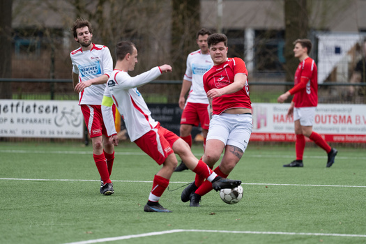 Youth soccer player in red jersey controlling ball while opponent in white jersey defends during match.