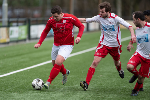 Youth soccer player in red jersey dribbling ball while being defended during match.