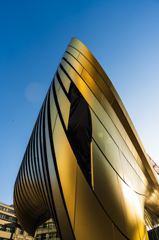 Modern curved architecture with golden and cream-colored metal panels against clear blue sky.