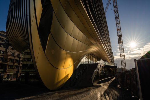 Modern curved architectural structure with golden-hour side lighting and dramatic shadows cast across pavement.