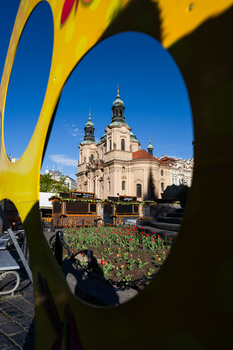 Eastern Orthodox cathedral with golden domes viewed through a yellow sculptural frame with red flowers in foreground.
