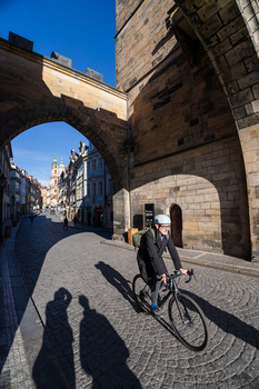 Cyclist riding through a historic stone archway on a European cobblestone street.