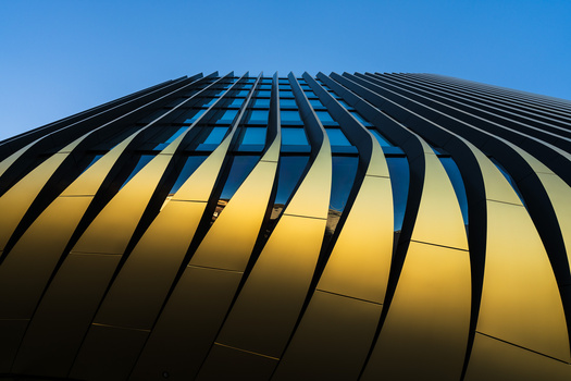 Modern curved building facade with yellow and black ribbed metal panels against clear blue sky.