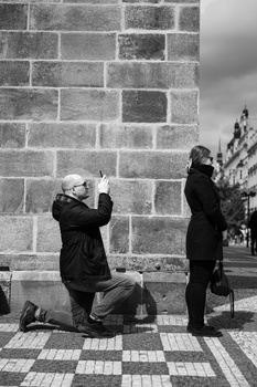 Photographer kneeling while shooting against a stone wall as another person stands nearby observing.