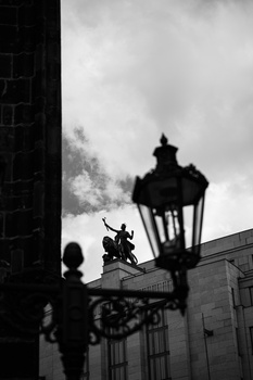 Silhouetted ornate street lamp against dramatic cloudy sky with building shadows.
