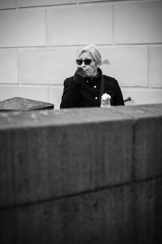Person wearing sunglasses and dark jacket seated at table with white brick wall background.