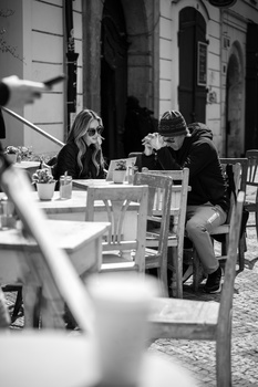 Two people seated at an outdoor café table at night, engaged in conversation under warm lighting.