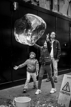Woman and child interacting with a large translucent spherical bubble against a dark urban wall.