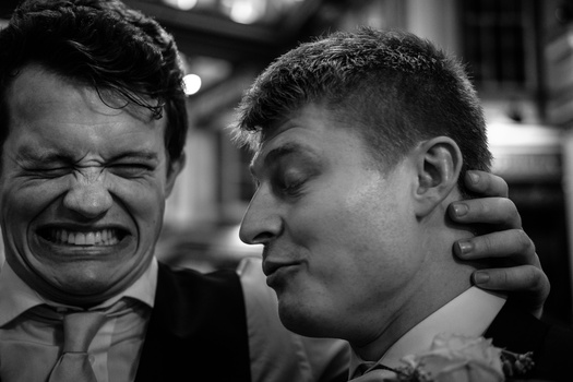 Two men in suits during an emotional moment, one smiling broadly while the other appears contemplative, captured in black and white.