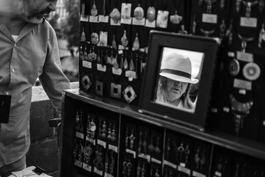 Photographer viewing a monitor displaying a portrait of a man wearing a white hat, with shelves of photography equipment visible in background.