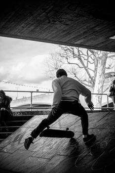 Athlete performing a parkour vault over a ledge beneath a covered structure, captured in black and white.