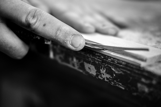 Close-up of a hand scraping paint from weathered wood with a metal tool.