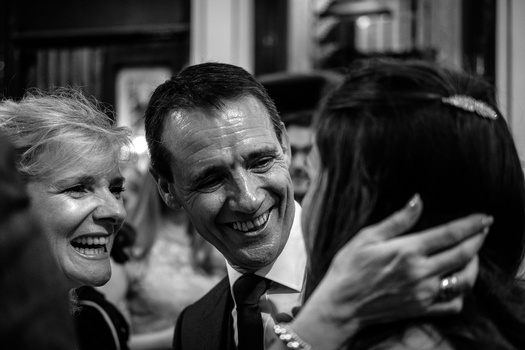 Three people at a formal event laughing together, captured in black and white portraiture.