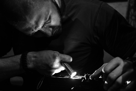 Jeweler examining a metal watch component under bright magnification light during detailed repair work.