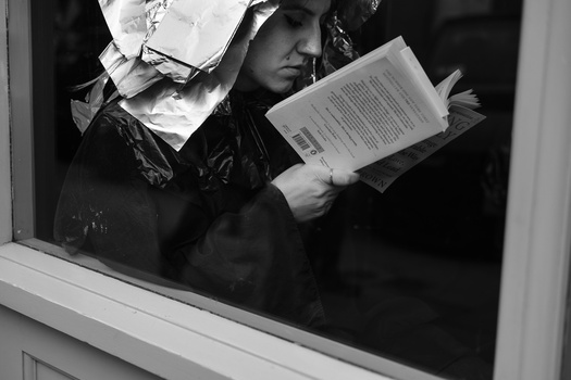 Person viewed through a window holding a document, shot in high-contrast black and white.