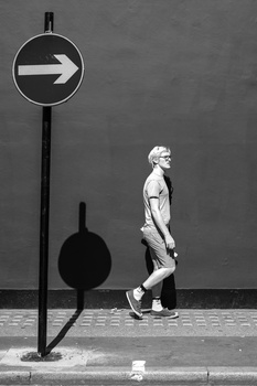 Black and white photograph of a jogger passing a directional arrow sign on an urban street.