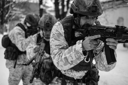 Soldier in winter camouflage uniform aiming rifle in snowy forest setting.