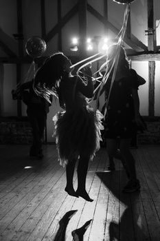 Two silhouetted figures holding large light modifiers in a studio with dramatic backlighting and shadows on wooden floor.
