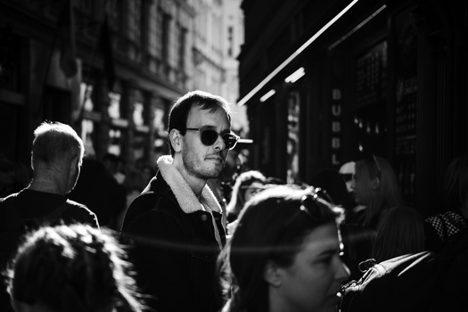 Man wearing sunglasses surrounded by people on a crowded urban street at night.