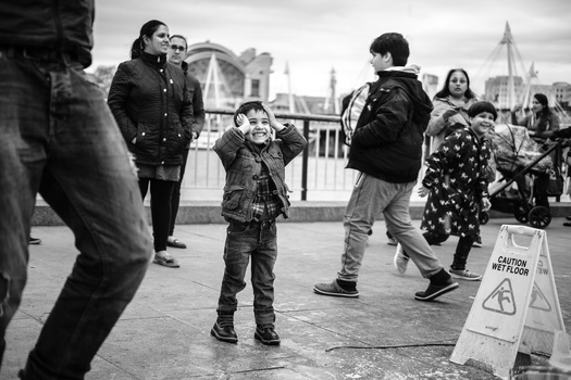 Child standing in public square surrounded by adults, captured in black and white street photography.