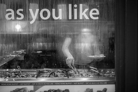 Black and white photograph of a person doing a handstand at a buffet counter, with repeating text overlay about eating volumes.