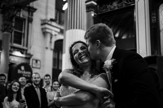 Bride and groom embracing and laughing during their wedding ceremony inside a classical building with columns.