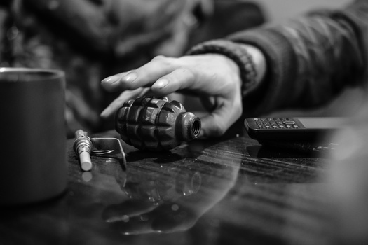 Hand holding a grenade on a wooden surface in black and white.
