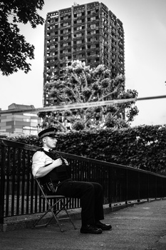Man in formal attire seated on a bench against urban high-rise backdrop in black and white.