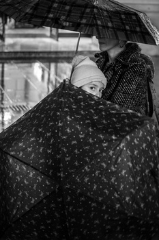 Person holding umbrellas in heavy rain, shot from below in black and white.