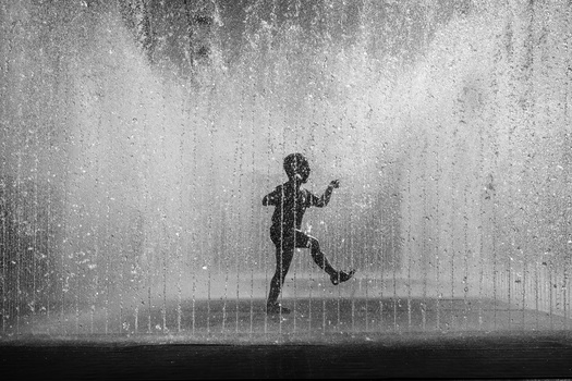 Silhouetted figure running through heavy rain against a concrete wall backdrop.