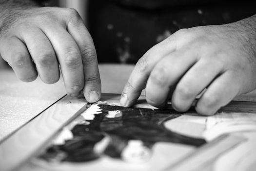 Two hands examining a black and white printed photograph or artwork on a light surface.
