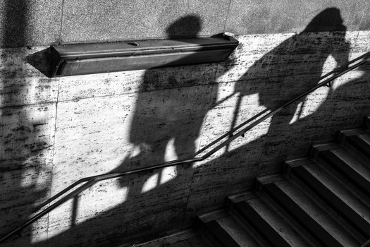 Silhouettes of people cast on a concrete wall with strong sunlight, creating dramatic shadows.