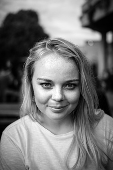 Young woman with long blonde hair smiling at camera in black and white portrait.