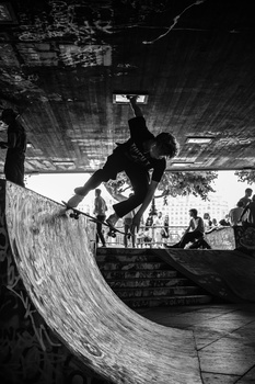 Skateboarder launching off a curved concrete ramp at a skate park in high-contrast black and white.