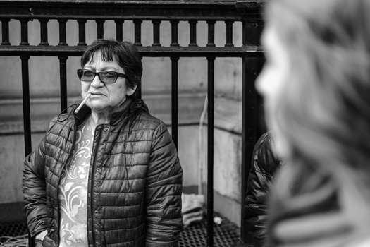 Man in glasses and quilted jacket gazes pensively to the side in black and white portrait.